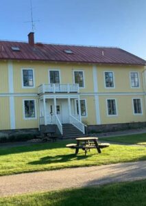 Vandrarhemmet på Evedals Camping, träbyggnad i gul panel med vita knutar och farstukvist.